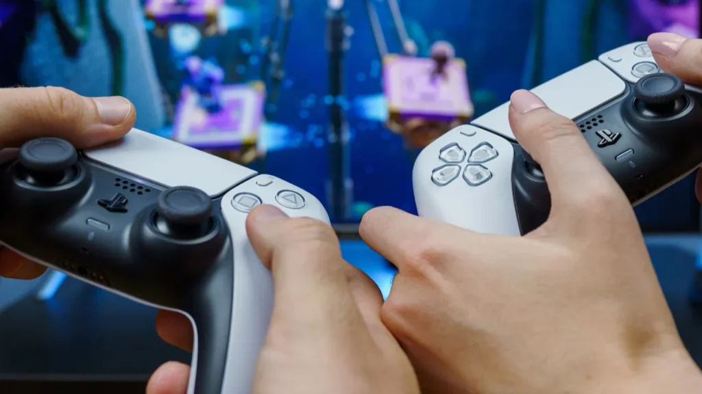 Hands holding PS5 controllers infront of the TV