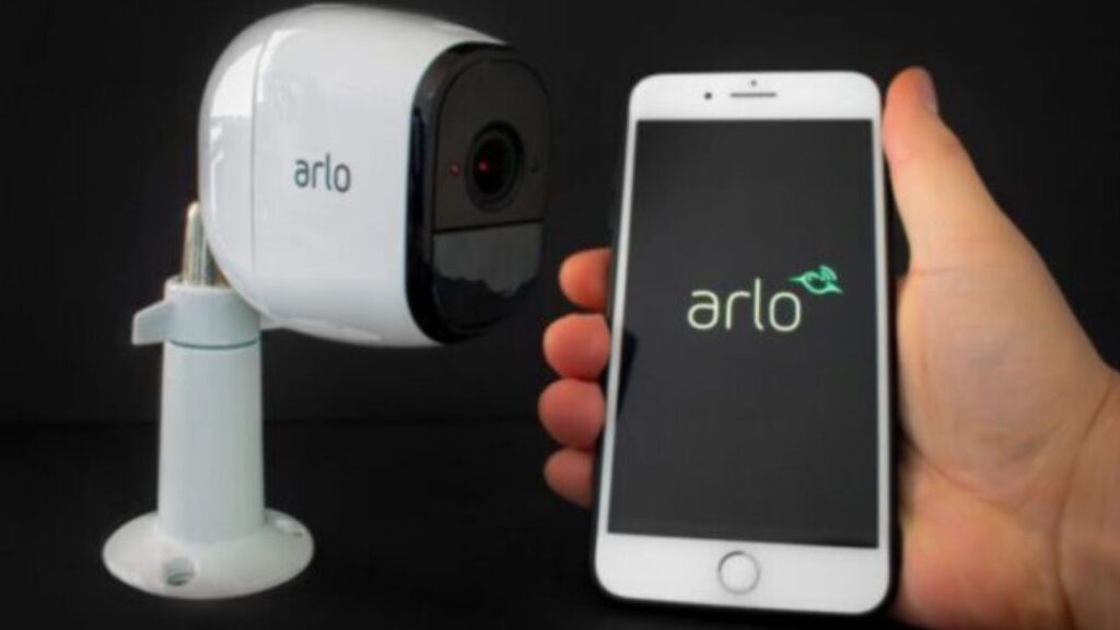 Arlo apsaugos kamera šalia išmaniojo telefono.