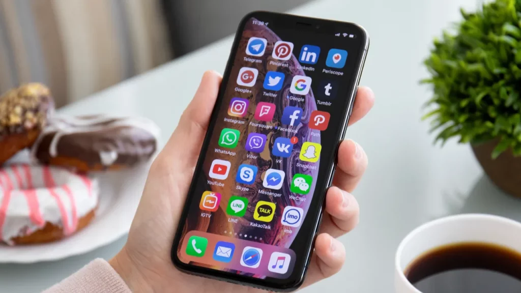 Ranka laiko išmanųjį telefoną, kuriame rodomos programų piktogramos.