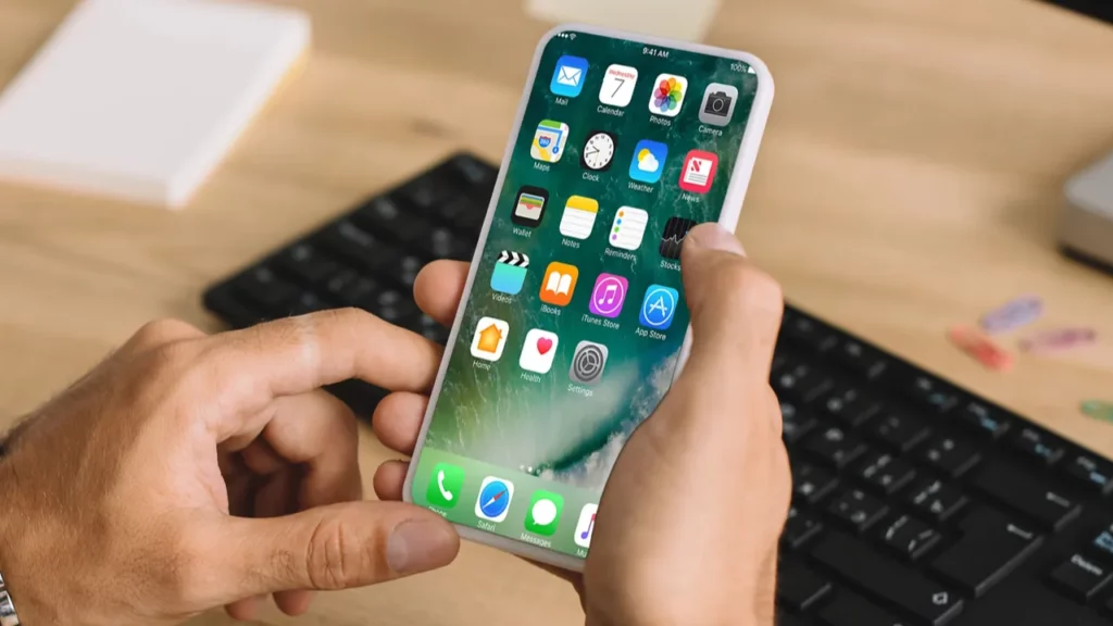 Rankos laikančios išmanųjį telefoną su programų piktogramomis.