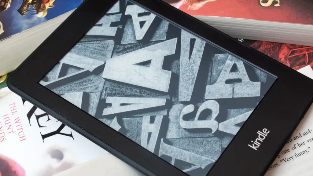 Kindle on books with letter art on screen.