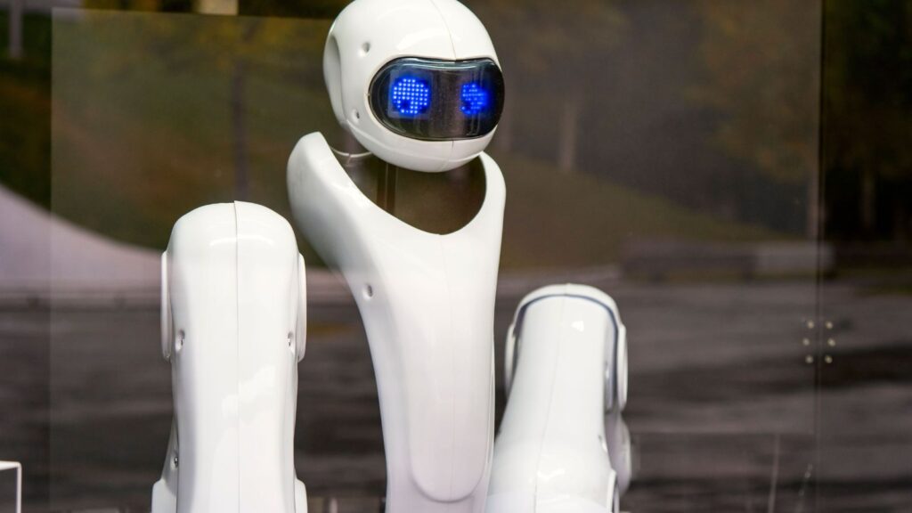 Baltas robotas mėlynomis akimis už stiklo.