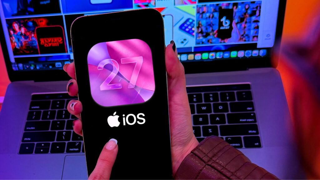 „iPhone“, kuriame priešais „MacBook“ rodoma „iOS 27“.
