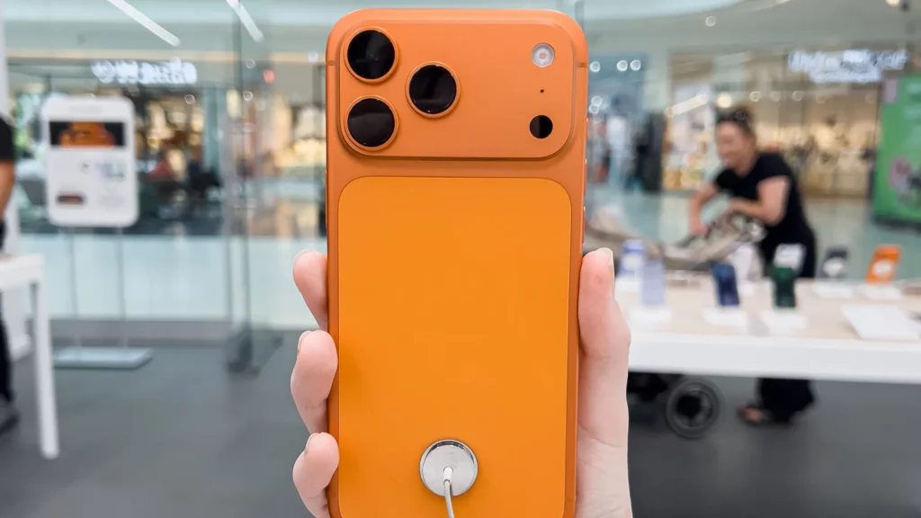 Oranžinės spalvos Apple išmanusis telefonas rankoje.